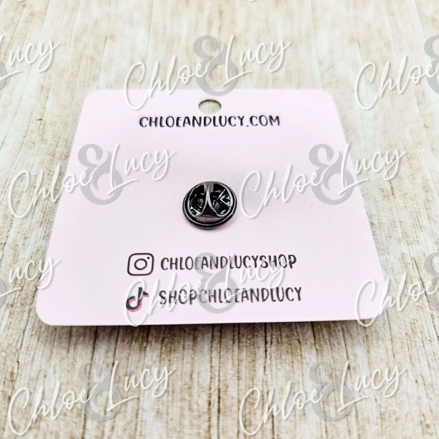 Small silver peace sign enamel pin on pink card, minimalist style, wood background