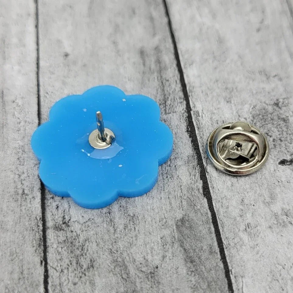 Blue flower-shaped enamel pin with metal backing on wooden surface