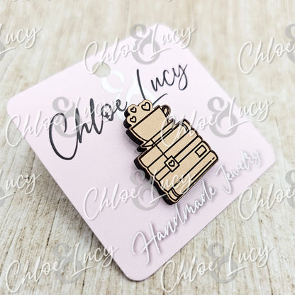 Wooden enamel pin with books and a heart mug on a light pink jewelry card