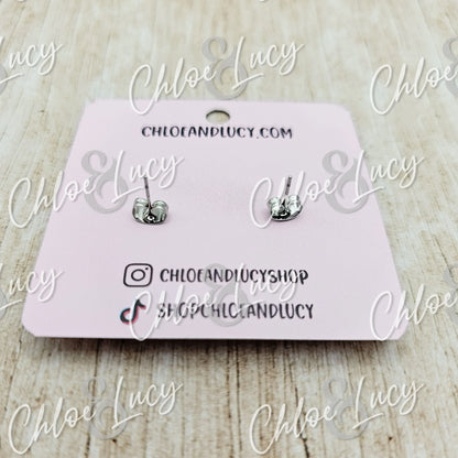 Silver knot stud earrings on a pink display card, minimalist jewelry on wooden background