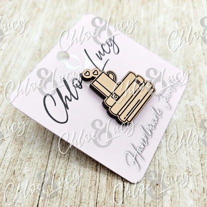 Wooden enamel pin shaped like a mug with books and hearts, on a display card