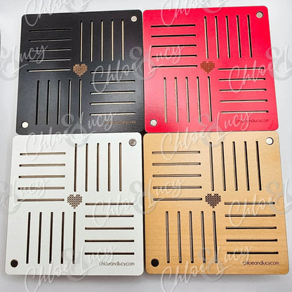 Set of four square wooden coasters in black, red, white, and natural, each with slotted cutouts and a small heart design.
