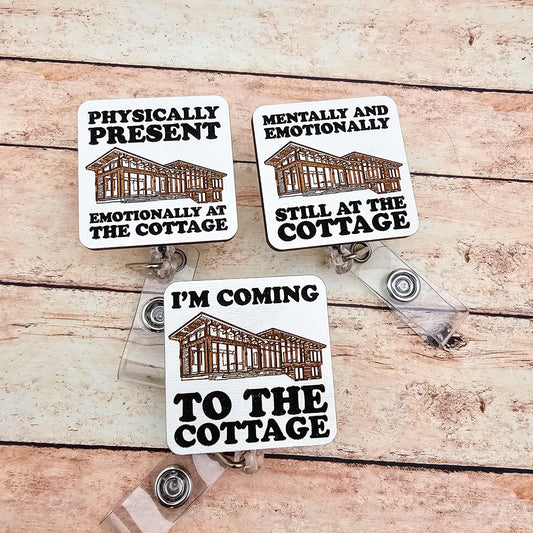 May include: Three white and brown cottage-themed badge reels with black text. The text on the badges reads: "Physically Present, Emotionally at the Cottage", "Mentally and Emotionally Still at the Cottage", and "I'm Coming to the Cottage".