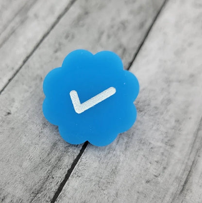 Blue flower-shaped pin with a white check mark on wood background