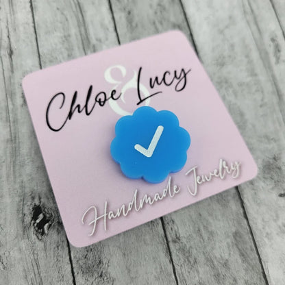 Blue scalloped acrylic pin with white check mark, displayed on pink handmade jewelry card