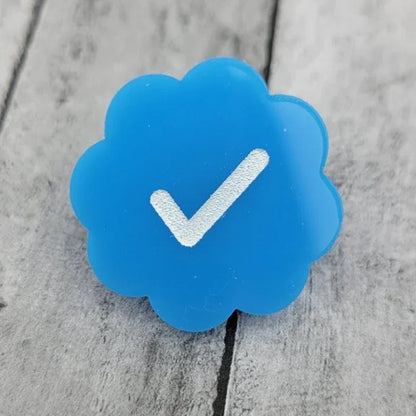 Blue flower-shaped pin badge with white check mark on wood background