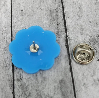 Blue flower-shaped enamel pin with metal clasp on wood background