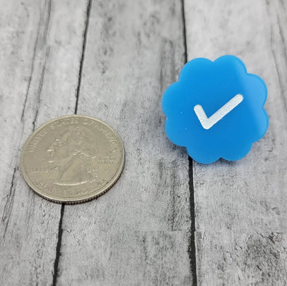 Blue checkmark badge pin next to a US quarter on a wood surface