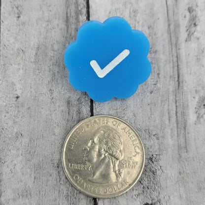 Blue checkmark pin shaped like a cloud next to a US quarter on wood background